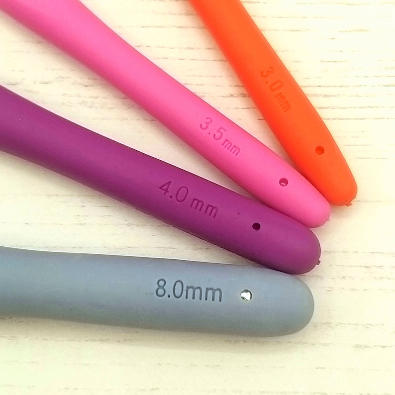 May include: Four silicone crochet hooks in different sizes and colors: orange (3.0 mm), pink (3.5 mm), purple (4.0 mm), and gray (8.0 mm).