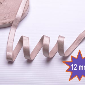 May include: A roll of 12 mm wide, beige elastic with a satin finish. The elastic is coiled and laid out on a white surface.