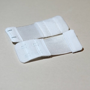 May include: Two white bra strap extenders with adjustable hooks. The extenders are made of a soft, stretchy fabric.