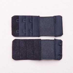 May include: Two black bra extenders with hook and eye closures. The extenders are made of a soft, stretchy fabric and have a hook and eye closure on one end and a row of hooks on the other end.
