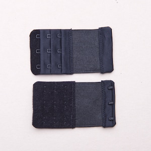 May include: Two black bra extenders with hook and eye closures. The top extender has three rows of hooks and the bottom extender has three rows of eyes.