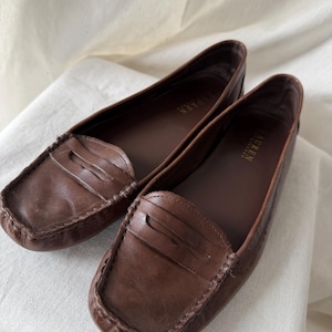 May include: A white ceramic mug with a black handle and the text "But First, Coffee" in a handwritten style. The mug is on a white surface. The mug is 10 cm tall.