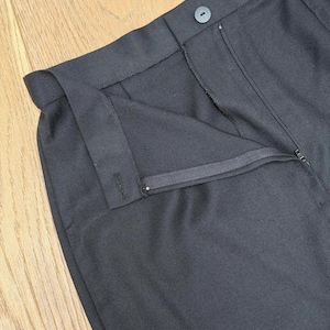Puede incluir: Un pantal&oacute;n negro liso que presenta una cintura estructurada con un cierre de bot&oacute;n a juego, una bragueta frontal con cremallera oculta y una confecci&oacute;n a medida con trabillas visibles para el cintur&oacute;n y costuras detalladas.