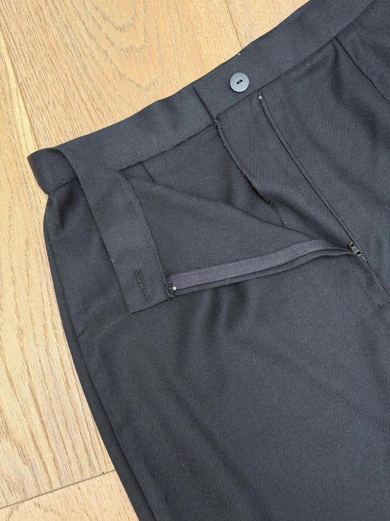 Puede incluir: Un pantal&oacute;n negro liso que presenta una cintura estructurada con un cierre de bot&oacute;n a juego, una bragueta frontal con cremallera oculta y una confecci&oacute;n a medida con trabillas visibles para el cintur&oacute;n y costuras detalladas.