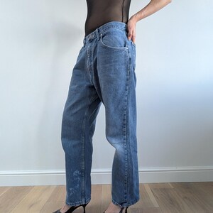 Op de afbeelding: Lichtblauwe jeans met een relaxte pasvorm. De jeans hebben een klassiek ontwerp met vijf zakken en een knoop- en ritssluiting. De jeans worden gecombineerd met zwarte pumps met spitse neus.
