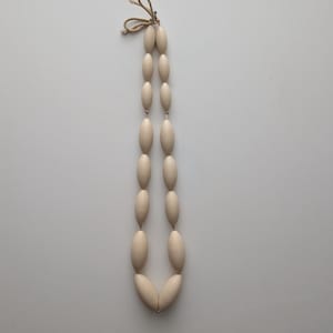 May include: Cream-colored beaded necklace with oval-shaped beads. The beads are strung together with a natural-colored cord, forming a long, elegant design. The necklace is displayed against a plain white background.