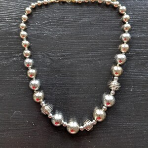 Peut inclure: Collier de perles argent&eacute;es avec fermoir &agrave; cha&icirc;ne dor&eacute;e. Le collier pr&eacute;sente un m&eacute;lange de grosses et petites perles rondes et brillantes argent&eacute;es, entrecoup&eacute;es de perles argent&eacute;es en forme de spirale.