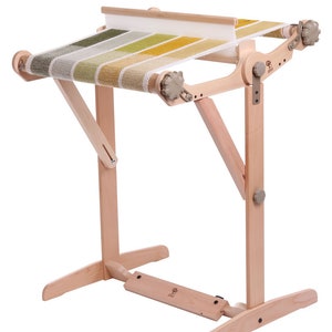 May include: A wooden loom with a stand, featuring a woven tapestry in shades of green and yellow.
