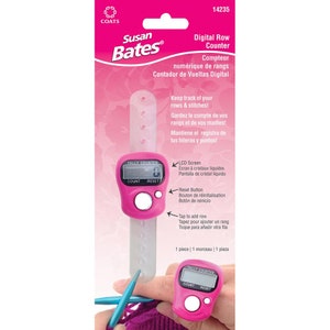 May include: Pink digital row counter with a clear LCD screen, count and reset buttons. The counter is attached to a clear plastic band and is being used to count rows of knitting.