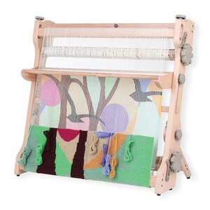 May include: A wooden tapestry loom with a colorful woven textile in progress. The textile features a design with pink, purple, and green shapes. The loom has adjustable knobs and a partially completed weaving project.