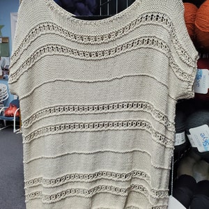 May include: A beige knitted top with a loose fit and short sleeves. The top has a delicate openwork pattern throughout, creating a light and airy feel.