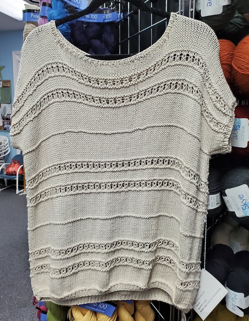 May include: A beige knitted top with a loose fit and short sleeves. The top has a delicate openwork pattern throughout, creating a light and airy feel.