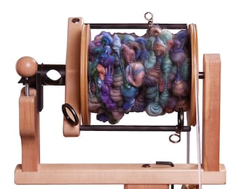 May include: A wooden spinning wheel with a large, colourful yarn ball on the spindle. The wheel has a wooden base and a metal arm that holds the spindle.