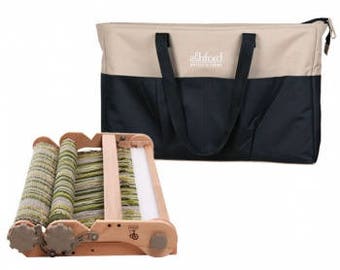 May include: A wooden loom with a green and white woven fabric on the warp. The loom is folded and has a carrying handle. A beige and black tote bag with the text "Ashford Handweaving" is also included.