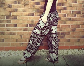 May include: A woman wearing a black vest top and black and white elephant print trousers. The trousers have a wide leg and a loose fit.