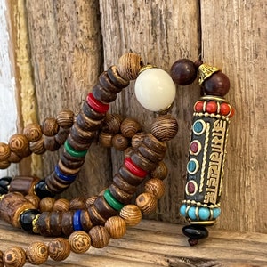 May include: A wooden beaded necklace with a white bead and a decorative pendant with a gold inscription and turquoise, red, and blue accents.