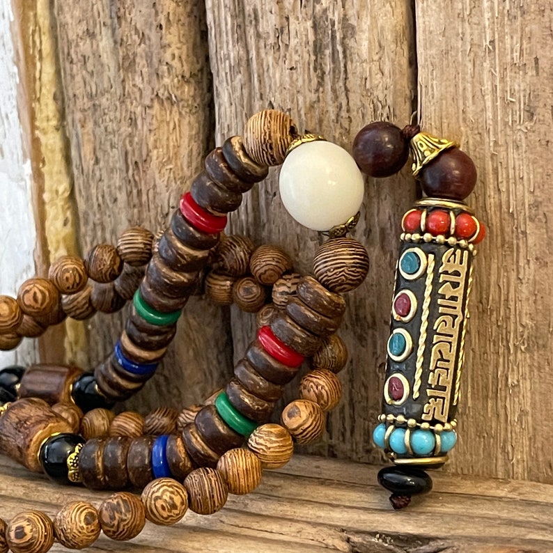 May include: A wooden beaded necklace with a white bead and a decorative pendant with a gold inscription and turquoise, red, and blue accents.