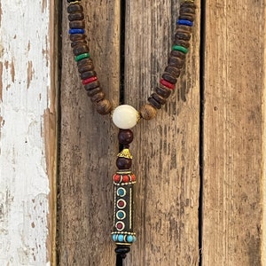 May include: A wooden beaded necklace with a white bead and a decorative pendant with red, blue, and gold accents.