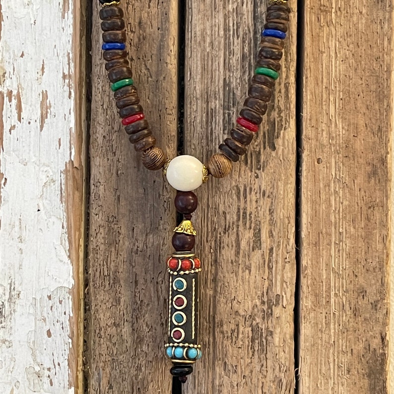 May include: A wooden beaded necklace with a white bead and a decorative pendant with red, blue, and gold accents.