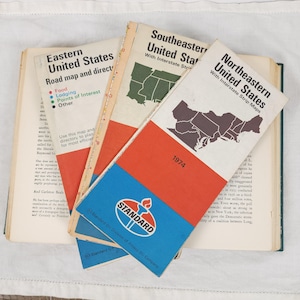 Puede incluir: Colección de mapas de carreteras antiguos de 1974, incluidos los Estados Unidos del Este, Sureste y Noreste. Los mapas presentan contornos estatales y el logotipo de Standard Oil. Los mapas están abiertos sobre un libro.