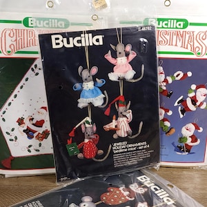 Könnte beinhalten: Ein Bucilla-Set zur Herstellung von "Jeweled Holiday Ornaments" mit "bedtime mice". Das Set enthält gestanzten Filz, Stickgarn und dekorative Verzierungen. Die Verpackung zeigt vier Mäuse-Ornamente in verschiedenen Outfits.