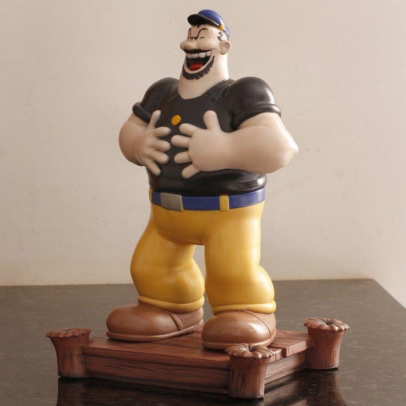 May include: A figurine of Popeye the Sailor Man, laughing with his hands on his stomach. He is wearing a blue sailor hat, a black shirt with a yellow button, and yellow pants. He is standing on a wooden base.
