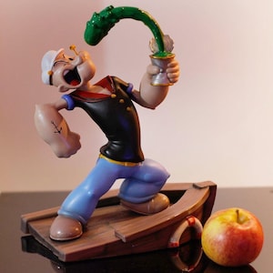 May include: A figurine of Popeye the Sailor Man, a cartoon character, in a blue sailor suit, holding a green spinach can and standing on a wooden boat. He has an anchor tattoo on his arm and is making a funny face.