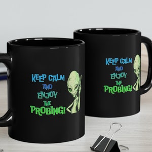 May include: Two black coffee mugs with a white alien graphic and the text "Keep Calm and Enjoy the Probing!" in blue and green text.