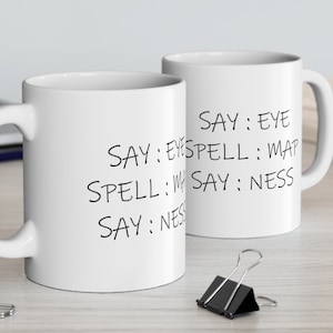Puede incluir: Dos tazas de cerámica blanca con texto negro que dice "SAY: EYE SAY: EYESPELL: MAP SPELL: SAY: NESS SAY: NES".