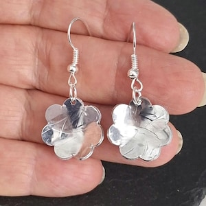 May include: A pair of silver flower earrings. Each earring has a five-petal floral design and a hook closure. The earrings are suspended from a coiled wire and a small bead.
