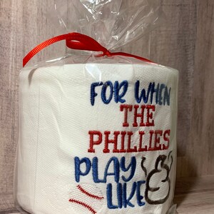 May include: A white toilet paper roll with red and blue embroidery that reads "For when the Phillies play like" with a baseball and a baseball glove graphic.