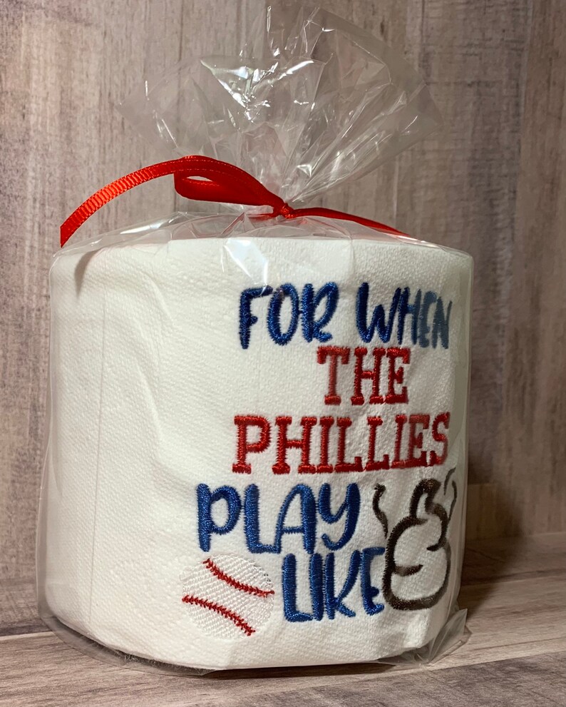May include: A white toilet paper roll with red and blue embroidery that reads "For when the Phillies play like" with a baseball and a baseball glove graphic.