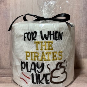 May include: A white toilet paper roll with a black ribbon and a clear plastic bag. The toilet paper has an embroidered design that says "For when the Pirates play like" with a baseball and a poop emoji.