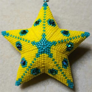 May include: A handmade, beaded star ornament in bright yellow and teal. The star is covered in small yellow beads with teal accents and iridescent gems. A teal star design is in the center. A small silver loop is at the top for hanging.