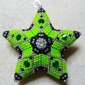 May include: A handmade beaded star ornament in a five-point design. The star features a vibrant neon green color with black and silver accents. Green crystals are embedded throughout the star. A silver loop is attached for hanging.