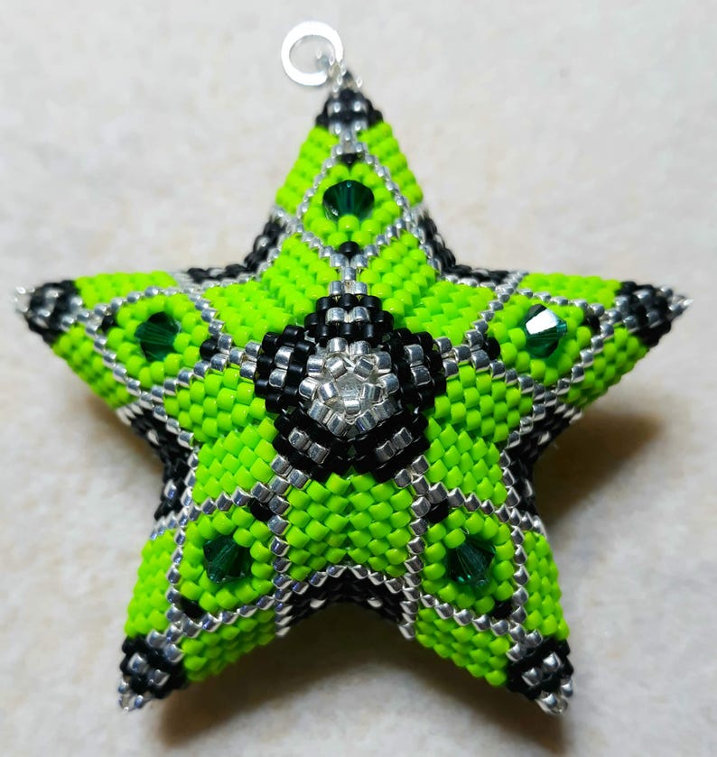 May include: A handmade beaded star ornament in a five-point design. The star features a vibrant neon green color with black and silver accents. Green crystals are embedded throughout the star. A silver loop is attached for hanging.