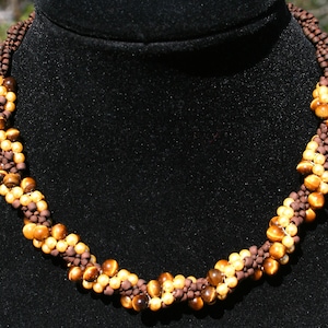 May include: A brown and gold beaded necklace with a twisted design. The beads are made of tiger's eye and brown glass.