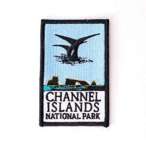 May include: A black and white embroidered patch with a blue background. The patch features a silhouette of a seabird flying over a rocky island. The text "CHANNEL ISLANDS NATIONAL PARK" is printed in black on a white background.