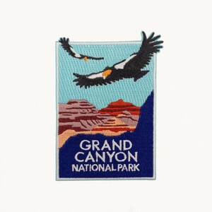 May include: A rectangular embroidered patch featuring a light blue sky with two black and white eagles in flight above layered red and brown canyon rock formations. The bottom section is dark blue with the white text GRAND CANYON NATIONAL PARK.