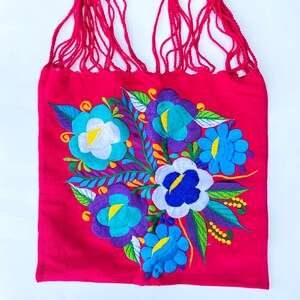 May include: A pink fabric tote bag with a floral embroidery design. The embroidery features blue, purple, white, and yellow flowers with green leaves.