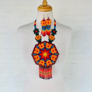 May include: A colorful beaded necklace and earrings set with a large, geometric, star-shaped pendant. The necklace features a red, orange, yellow, blue, and green color scheme with black beads outlining the design. The earrings are smaller versions of the pendant.