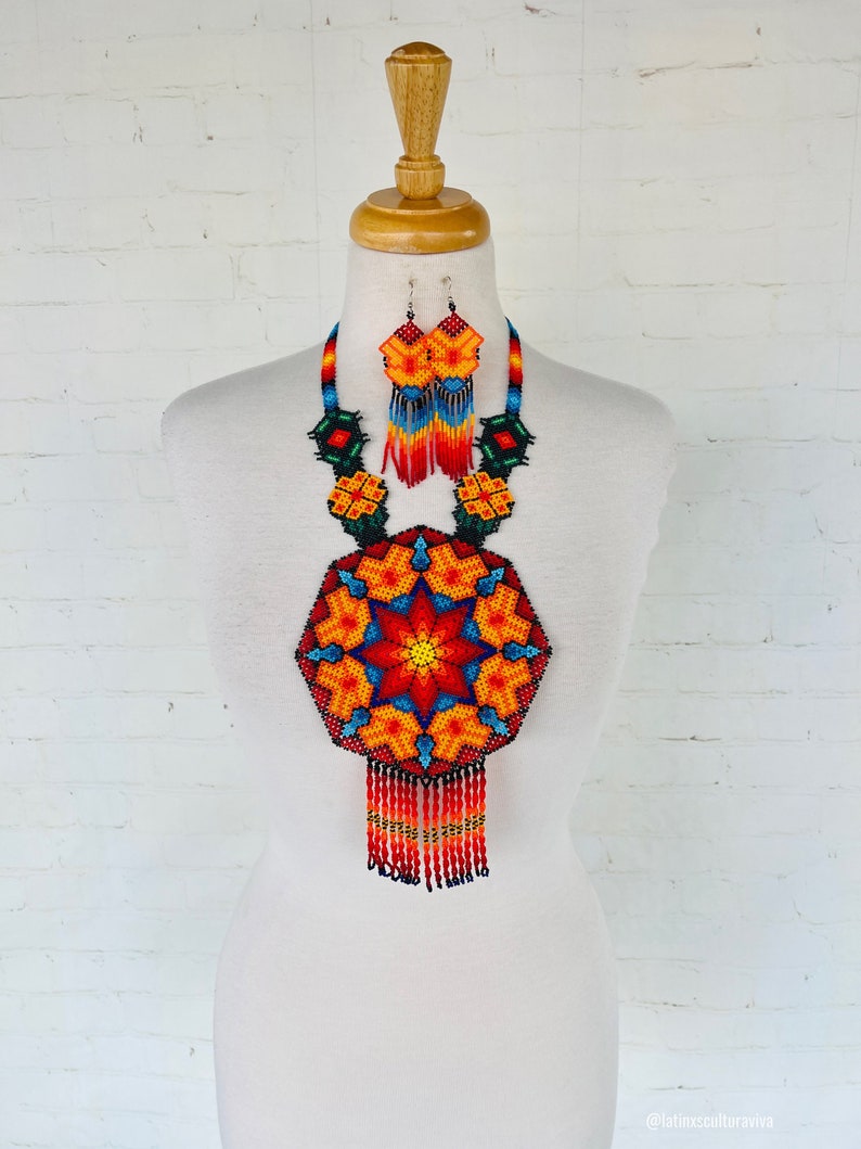 May include: A colorful beaded necklace and earrings set with a large, geometric, star-shaped pendant. The necklace features a red, orange, yellow, blue, and green color scheme with black beads outlining the design. The earrings are smaller versions of the pendant.