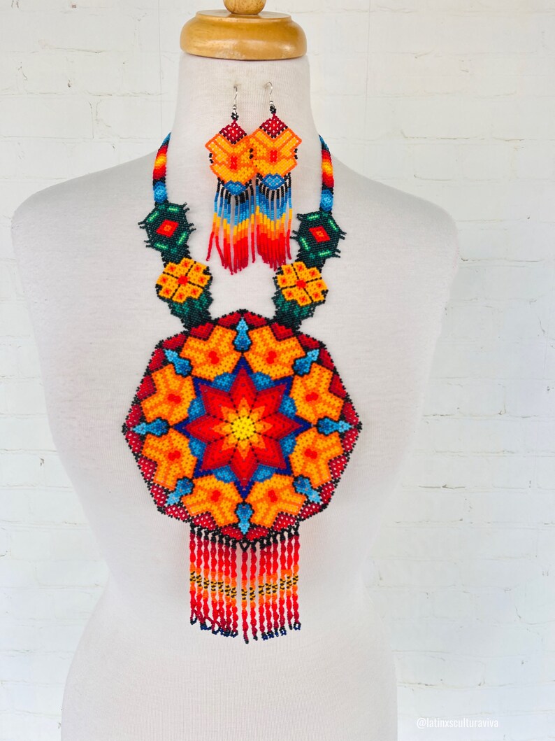 May include: A colorful beaded necklace and earrings set with a large, round pendant featuring a starburst design in shades of red, orange, yellow, blue, and green. The necklace has a fringe of beads.