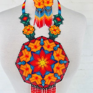 May include: A colorful beaded necklace and earrings set with a large, round pendant featuring a starburst design in shades of red, orange, yellow, blue, and green. The pendant has a fringe of red beads.
