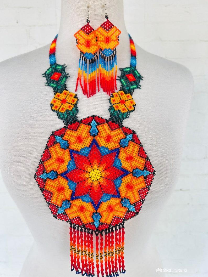 May include: A colorful beaded necklace and earrings set with a large, round pendant featuring a starburst design in shades of red, orange, yellow, blue, and green. The pendant has a fringe of red beads.