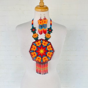 May include: A colorful beaded necklace and earrings set with a geometric design in shades of red, orange, yellow, blue, and green. The necklace features a large, round pendant with a starburst pattern and a fringe of beads.