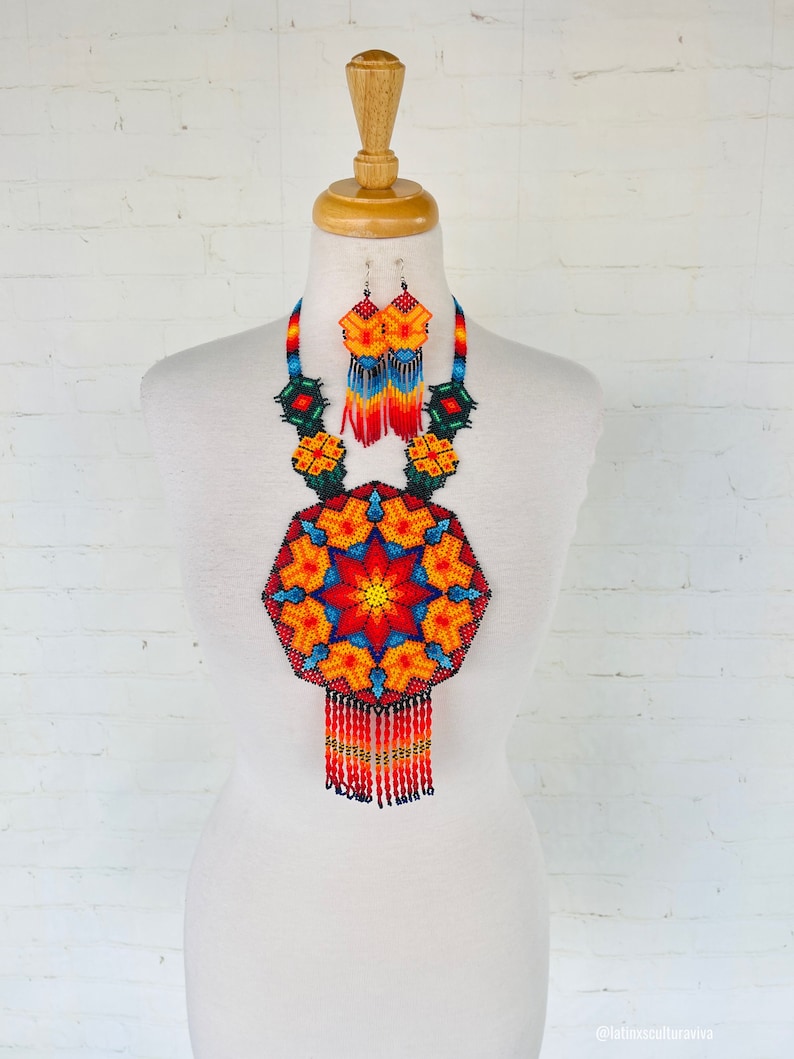 May include: A colorful beaded necklace and earrings set with a geometric design in shades of red, orange, yellow, blue, and green. The necklace features a large, round pendant with a starburst pattern and a fringe of beads.