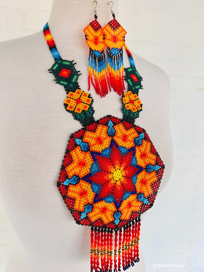 May include: A colorful beaded necklace and earrings set with a large, round pendant featuring a starburst design in red, orange, yellow, blue, and black. The pendant has a fringe of red beads.