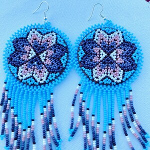 K&ouml;nnte beinhalten: Ein Paar Perlenohrringe mit einem floralen Design in Blau, Wei&szlig;, Rosa und Braun. Die Ohrringe haben einen Fransen aus blauen, wei&szlig;en, rosa und braunen Perlen.