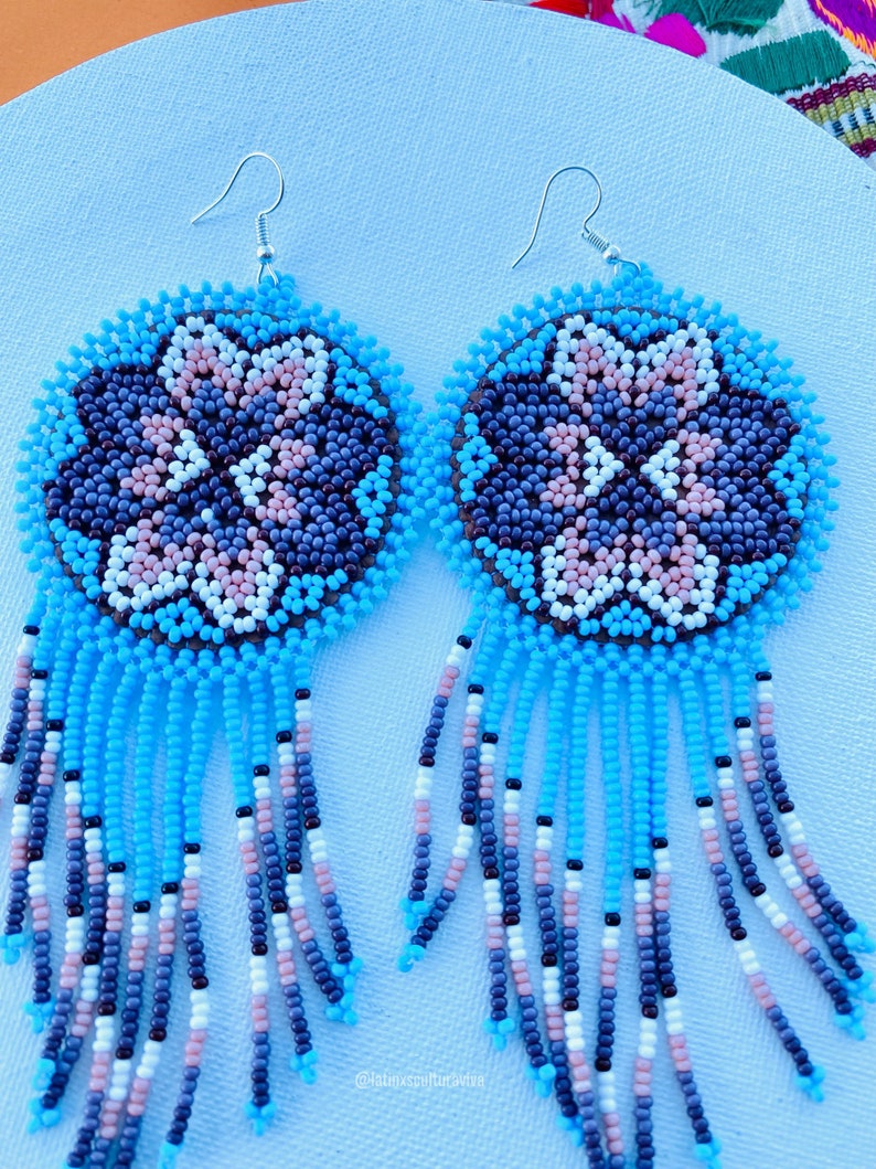 K&ouml;nnte beinhalten: Ein Paar Perlenohrringe mit einem floralen Design in Blau, Wei&szlig;, Rosa und Braun. Die Ohrringe haben einen Fransen aus blauen, wei&szlig;en, rosa und braunen Perlen.